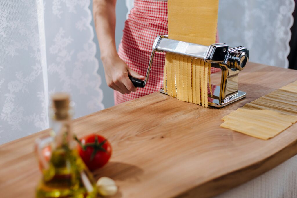 A woman in a red apron using a pasta maker to prepare fresh Italian pasta.